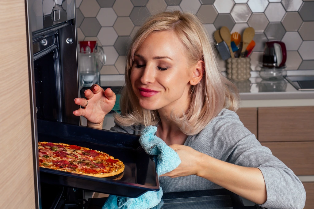 Rosa Sterling smiling with her eyes closed, smelling a freshly baked pepperoni pizza she is taking out of the oven.