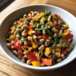 A white bowl filled with colorful Black-eyed pea salad mixed with diced red and yellow bell peppers and fresh herbs.