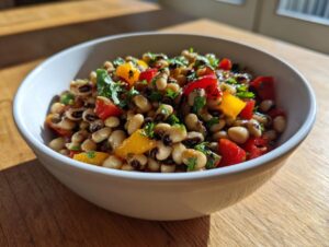 A close-up of a vibrant Black-eyed pea salad mixed with chopped red and yellow bell peppers and fresh herbs in a white bowl.