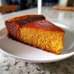 A thick, golden-orange slice of crustless pumpkin pie with a deeply caramelized top, served on a white plate.