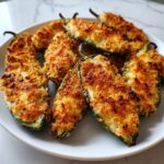 A plate piled high with baked Jalapeño poppers featuring a crispy, golden-brown breadcrumb topping.