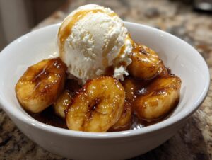 A white bowl filled with caramelized bananas and a large scoop of vanilla ice cream, ready for Bananas Foster.