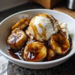 Close-up of a bowl of Bananas Foster featuring caramelized bananas, rich sauce, and a scoop of vanilla ice cream.