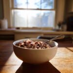 A creamy bowl of black eyed peas recipe with bits of meat, sitting on a sunlit wooden table.