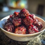 A white bowl filled with glistening, dark red Grape Jelly Meatballs stacked high.
