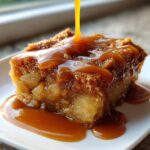 Close-up of a square slice of caramel apple dump cake being generously drizzled with thick, golden caramel sauce.
