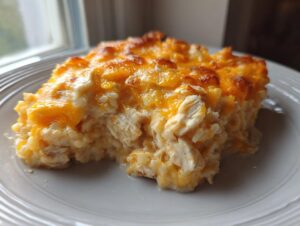 A close-up of a serving of cheesy chicken and rice casserole with a golden, melted cheddar topping.