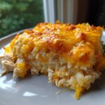 A generous serving of cheesy chicken and rice casserole with a golden, melted cheddar topping.