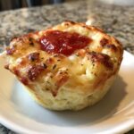 A single, golden-brown pizza muffin topped with melted cheese and a dollop of red pizza sauce.