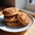 A stack of four chewy Snickerdoodle cookies coated in cinnamon sugar, resting on a white plate.