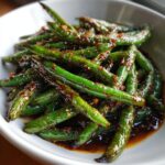 Vibrant green beans coated in a rich, dark chinese garlic sauce, served in a white bowl.