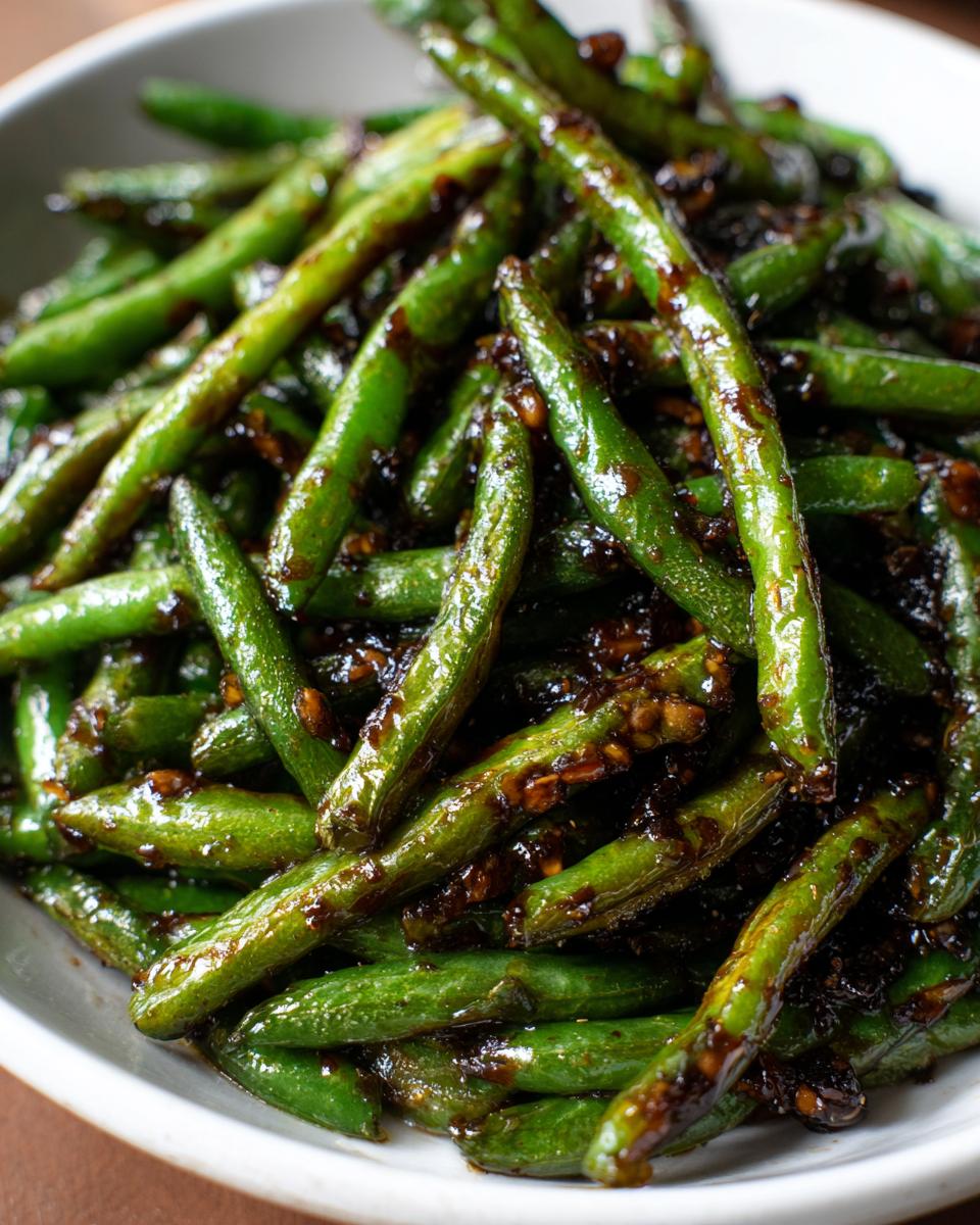 A close-up shot of bright green, blistered chinese green beans with garlic sauce coating them.