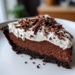 A rich slice of Christmas chocolate cream pie featuring a dark crust, thick chocolate filling, and whipped cream topped with chocolate shavings.