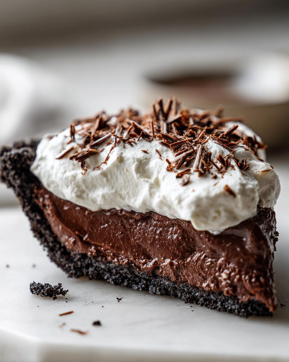 A decadent slice of Christmas chocolate cream pie featuring a dark crust, rich filling, whipped cream, and chocolate shavings.