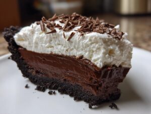Close-up of a rich slice of Christmas chocolate cream pie with a dark crust, thick chocolate filling, and whipped cream topped with chocolate shavings.