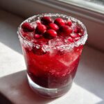 A vibrant cranberry pomegranate margarita in a sugar-rimmed glass, topped with fresh cranberries and pomegranate seeds.