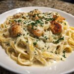 A close-up shot of creamy chicken alfredo pasta served in a white bowl, topped with grilled chicken pieces and fresh parsley.