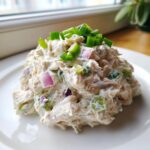 A mound of creamy cottage cheese chicken salad mixed with red onion and celery, topped with fresh green chives.