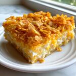 A close-up slice of creamy, cheesy hashbrown casserole topped generously with crunchy golden cornflakes.