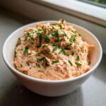 A white bowl filled with creamy, pinkish salmon dip, generously garnished with chopped green chives.