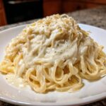 Close-up of fettuccine pasta generously coated in rich homemade alfredo sauce and topped with grated Parmesan.