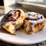 Close-up of a fluffy, freshly baked cinnamon roll cut in half, showing the soft interior and dripping white icing.