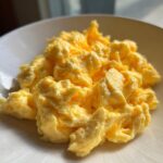 Close-up of perfectly fluffy, creamy yellow scrambled eggs served in a white bowl.