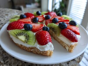A slice removed from a vibrant fruit pizza sugar cookie topped with cream cheese frosting, strawberries, kiwi, and blueberries.