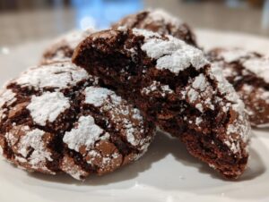 Close-up of fudgy chocolate crinkle cookies dusted heavily with powdered sugar, one cookie is broken open.