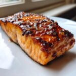 Close-up of a perfectly cooked, glistening honey garlic salmon fillet on a white plate.
