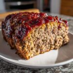 Close-up of a moist slice of Keto meatloaf topped with a thick, shiny red glaze.