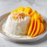 A perfectly molded serving of mango sticky rice with sliced fresh mango and toasted coconut flakes.
