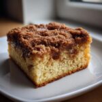 Close-up of a moist slice of coffee cake featuring a thick, sugary cinnamon crumb topping.