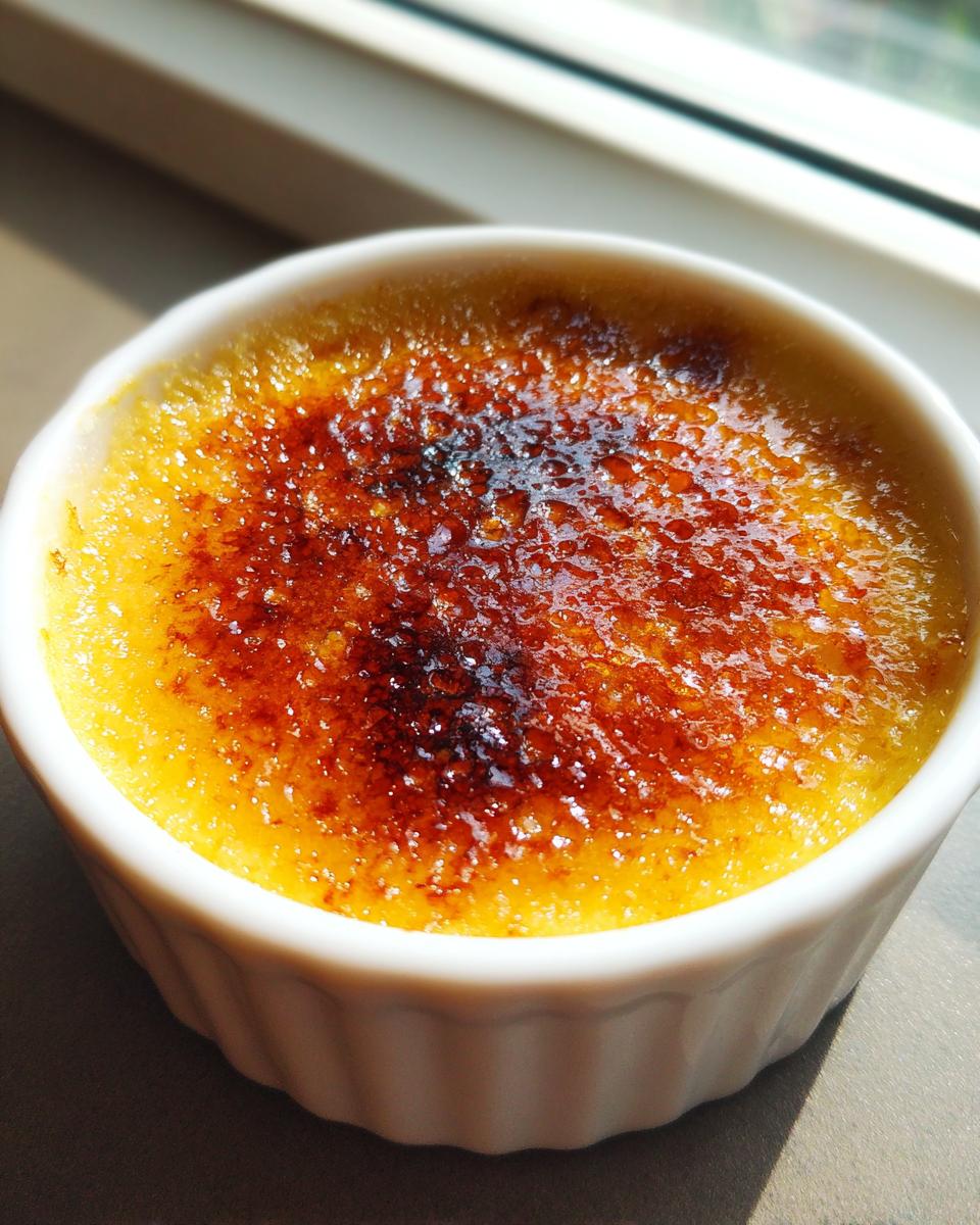 Close-up of a classic Creme Brulee in a white ramekin showing the perfectly caramelized, crackly sugar topping.