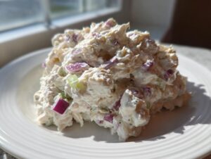 A mound of creamy cottage cheese chicken salad mixed with visible chunks of red onion and celery on a white plate.