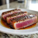 Three thick slices of seared tuna steak, perfectly rare inside, crusted with sesame seeds and sitting in a savory marinade.