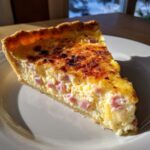 A perfect slice of ham and cheese quiche showing creamy filling, diced ham, and a beautifully browned top.
