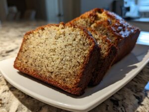 Close-up of moist, sliced sugar free banana bread with a golden-brown crust on a white serving dish.