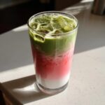 A tall glass showcasing a vibrant strawberry matcha latte with distinct layers of white milk, pink strawberry puree, and green matcha.