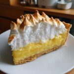 Close-up of a thick slice of lemon meringue pie showing bright yellow curd and towering, toasted meringue peaks.