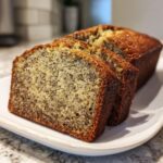 Two thick slices of moist sugar free banana bread studded with poppy seeds, resting on a white plate.