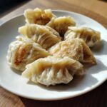 A plate of golden-brown, pan-fried Traditional Chinese Dumplings glistening under sunlight.