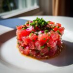 Close-up of a perfectly molded Tuna Tartare Recipe stack garnished with red onion and chives.