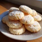 A stack of freshly baked 3-ingredient butter cookies dusted generously with powdered sugar on a white plate.