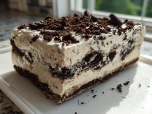 A rectangular slice of rich Oreo dirt cake showing distinct layers of cream and crushed chocolate cookies.
