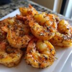 Close-up of perfectly cooked air fryer frozen shrimp seasoned with herbs and spices on a white plate.