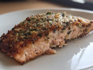 Close-up of a flaky, moist piece of air fryer salmon topped with a golden garlic and herb crust.