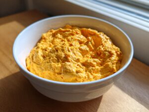 A close-up of thick, vibrant orange beer cheese dip served in a white bowl on a wooden surface.