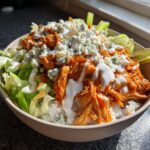 A close-up of an amazing buffalo chicken bowl featuring shredded chicken, white rice, lettuce, blue cheese crumbles, and ranch dressing.