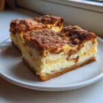 Close-up of two squares of amazing churro cheesecake with a thick cream cheese layer and cinnamon-sugar topping.